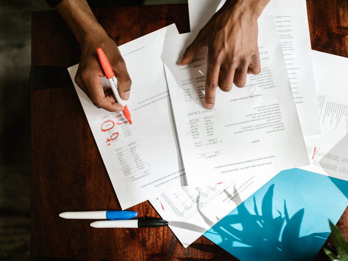 Hands marking up printed reports with a pen on a desk
